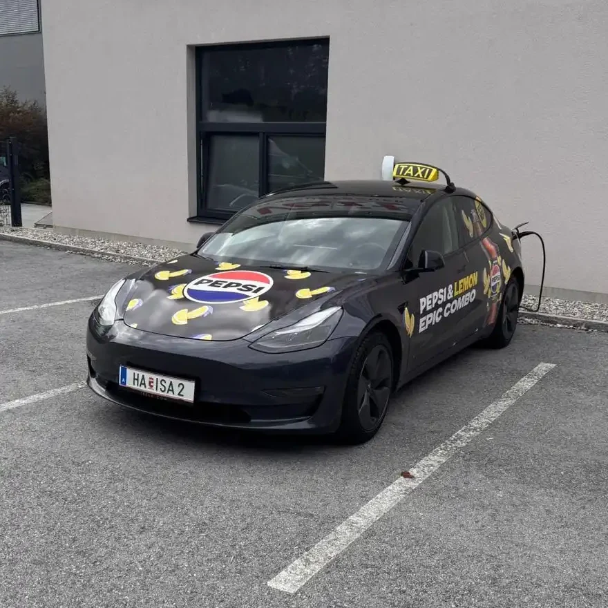 Tesla Taxi von Taxi Hallein mit Pepsi & Lemon Werbung lädt am Firmenparkplatz
